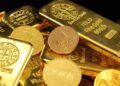 Lingotes de oro apilados en una bóveda, con cotización en pantalla al fondo