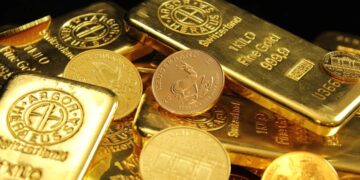 Lingotes de oro apilados en una bóveda, con cotización en pantalla al fondo