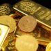 Lingotes de oro apilados en una bóveda, con cotización en pantalla al fondo