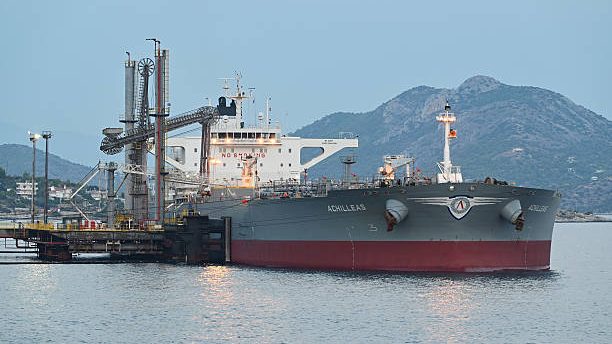 Plataforma petrolera con barriles de crudo WTI mientras operadores siguen la caída del precio del petróleo en pantallas de mercado