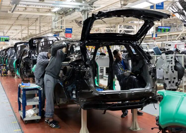 Línea de ensamblaje de vehículos en una planta automotriz de México con trabajadores y brazos robóticos