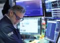 Pantalla de cotizaciones mostrando caídas en el Nasdaq y el S&P 500 con operadores en la Bolsa de Nueva York