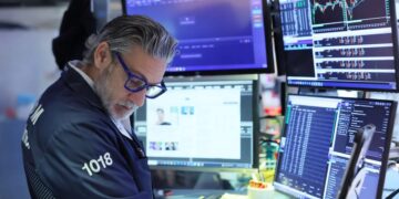 Pantalla de cotizaciones mostrando caídas en el Nasdaq y el S&P 500 con operadores en la Bolsa de Nueva York