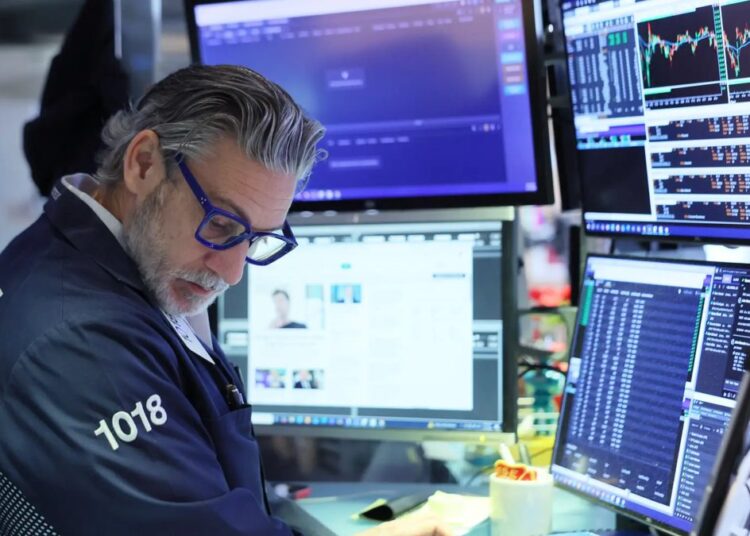 Pantalla de cotizaciones mostrando caídas en el Nasdaq y el S&P 500 con operadores en la Bolsa de Nueva York