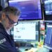 Pantalla de cotizaciones mostrando caídas en el Nasdaq y el S&P 500 con operadores en la Bolsa de Nueva York