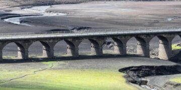 Cauce seco de un río europeo en verano con barcazas varadas y tierra agrietada visible en la orilla