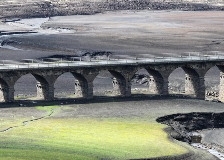 Cauce seco de un río europeo en verano con barcazas varadas y tierra agrietada visible en la orilla