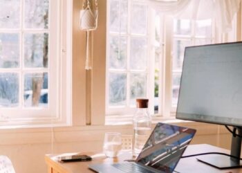 Persona trabajando frente a una computadora de escritorio en una oficina moderna junto a una laptop cerrada sobre el escritorio