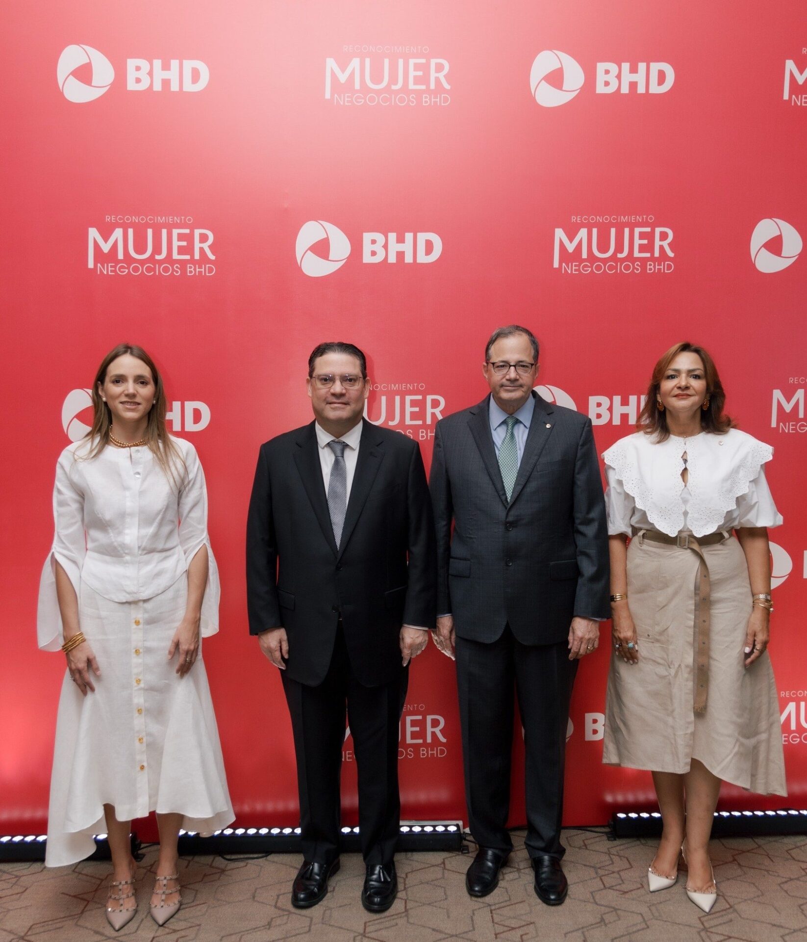 Cuatro ejecutivos del Banco BHD posan ante un telón rojo del evento Reconocimiento Mujer Negocios BHD.
