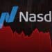 Pantalla del Nasdaq en Times Square mostrando caída bursátil con operadores en Wall Street al fondo