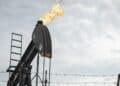Barriles de petróleo apilados en una refinería con indicadores de precios al alza en pantallas de mercado