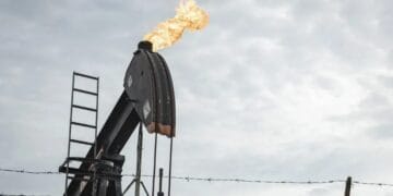 Barriles de petróleo apilados en una refinería con indicadores de precios al alza en pantallas de mercado