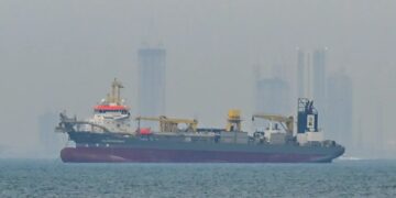 Superpetrolero cargado de crudo navegando por el Estrecho de Ormuz con instalaciones petroleras al fondo