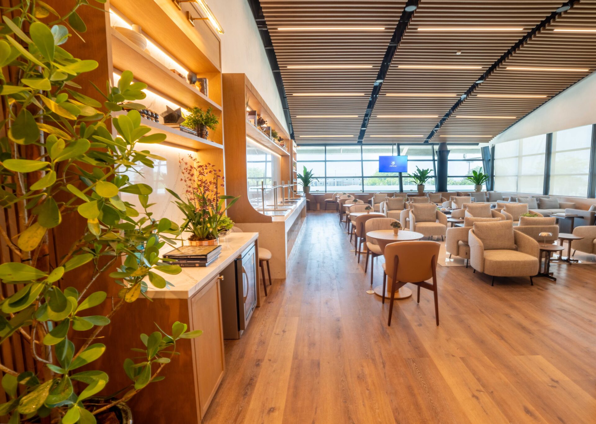 Interior luminoso de la nueva sala VIP del Lounge Popular en el AILA, con sillones beige, piso de madera y plantas