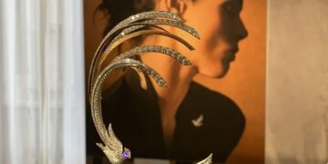 Lingotes de oro, joyas y reloj de lujo sobre superficie reflectante, representando activos tangibles de inversión