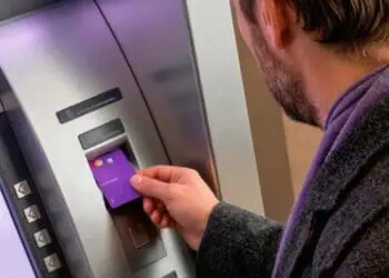 Tarjeta Nu morada sobre pantalla de cajero automático mostrando comisión de retiro de efectivo