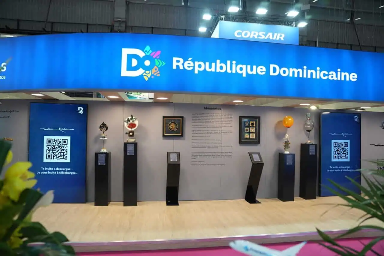Stand de República Dominicana en una feria internacional de turismo con esculturas decorativas, códigos QR y el logo del