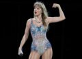 Taylor Swift en el escenario durante la gira The Eras Tour, sosteniendo una guitarra rosa con botas plateadas y luces moradas de fondo