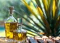 Botellas de tequila mexicano alineadas en una destilería, con agave azul al fondo