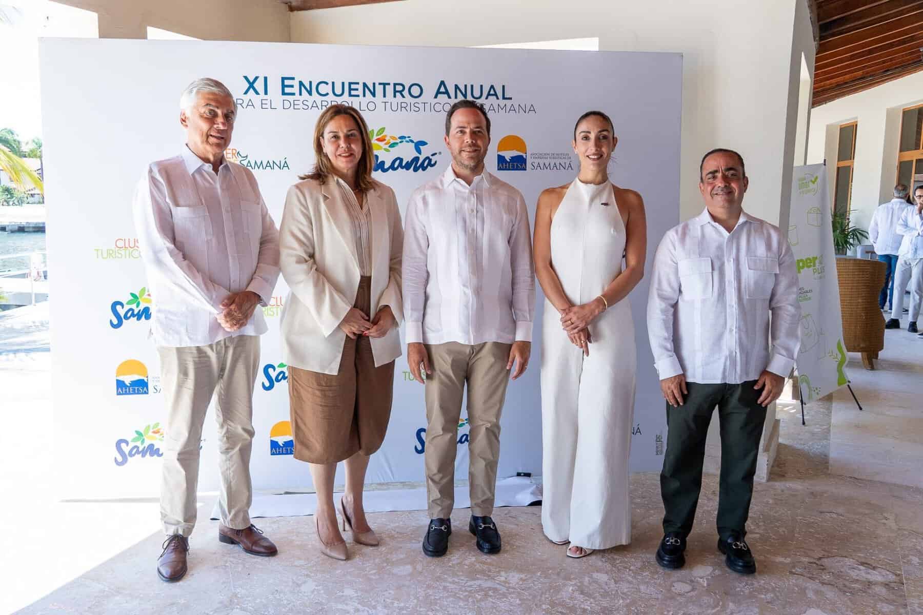 Cinco asistentes al XI Encuentro Turístico de Samaná posan ante el panel oficial del evento.