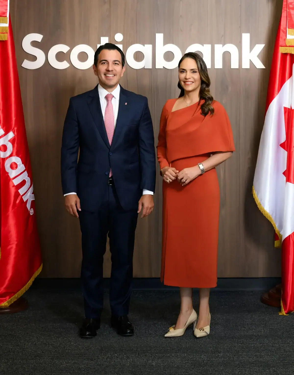 Dos ejecutivos de Scotiabank posan ante el logo y banderas de la institución bancaria.