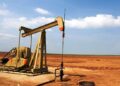 Plataforma de extracción de petróleo con humo en el horizonte y cielo nublado, evocando tensión en mercados energéticos