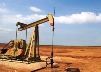 Plataforma de extracción de petróleo con humo en el horizonte y cielo nublado, evocando tensión en mercados energéticos