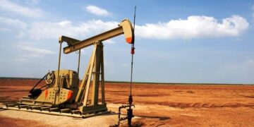 Plataforma de extracción de petróleo con humo en el horizonte y cielo nublado, evocando tensión en mercados energéticos