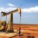 Plataforma de extracción de petróleo con humo en el horizonte y cielo nublado, evocando tensión en mercados energéticos