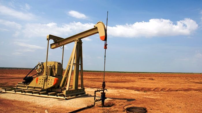 Plataforma de extracción de petróleo con humo en el horizonte y cielo nublado, evocando tensión en mercados energéticos
