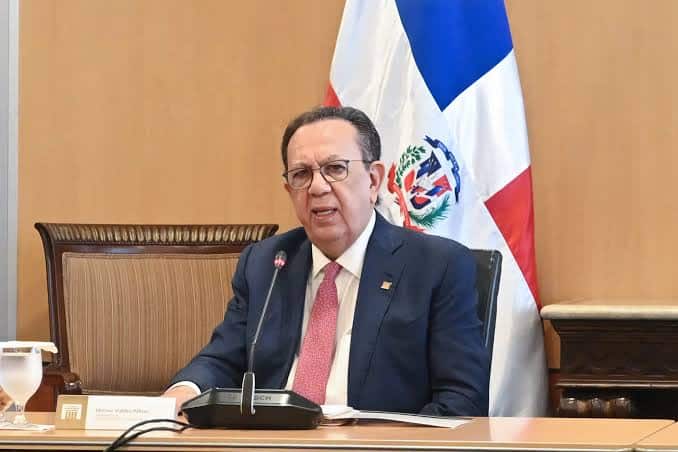 Funcionario del BCRD habla ante micrófono con la bandera dominicana al fondo.