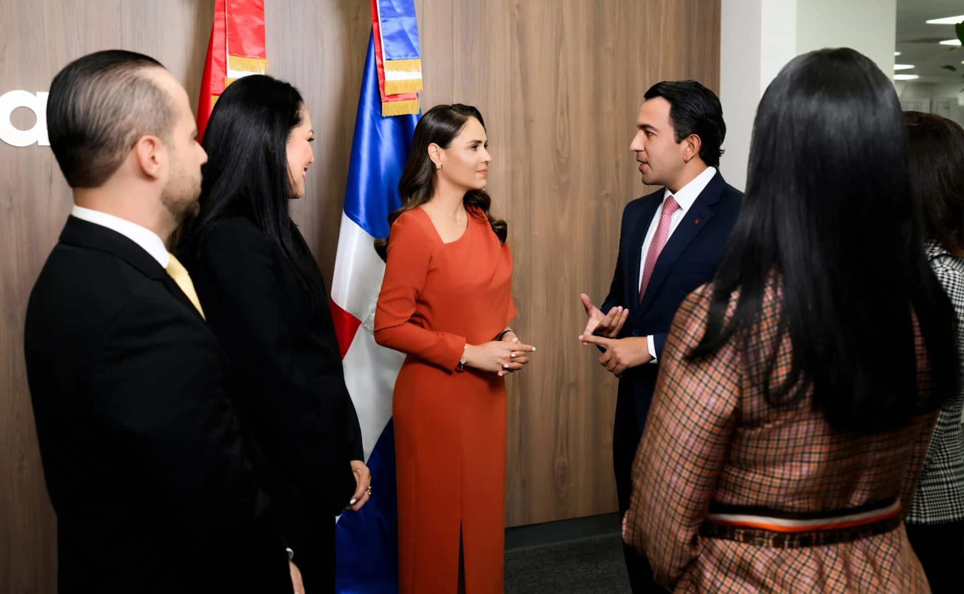 Grupo de profesionales conversa frente a banderas de la República Dominicana en un evento corporativo.