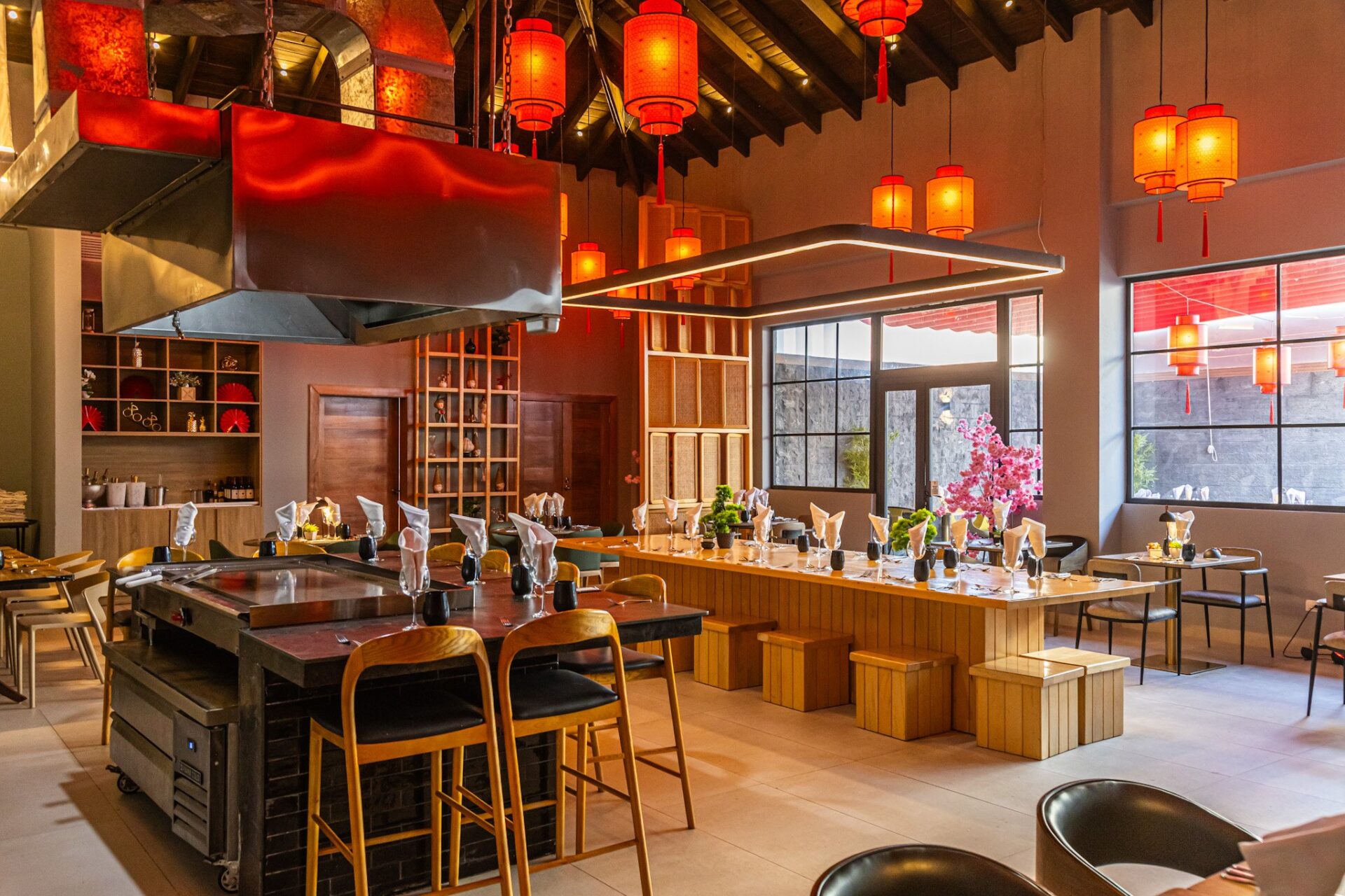 Interior de restaurante asiático decorado con linternas rojas chinas colgantes, mesas de teppanyaki y barra de madera