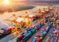 Contenedores de carga en un puerto chino con grúas industriales y barcos de exportación al fondo