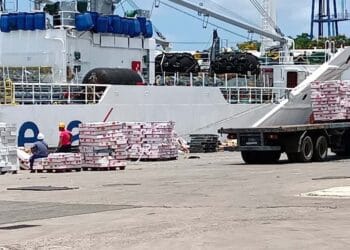Barco de carga frente al puerto de La Habana, Cuba, con banderas de Estados Unidos y Cuba al fondo