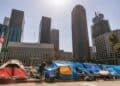 Personas sin hogar en carpas en una calle de Los Ángeles, California, con edificios de apartamentos al fondo