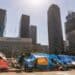 Personas sin hogar en carpas en una calle de Los Ángeles, California, con edificios de apartamentos al fondo
