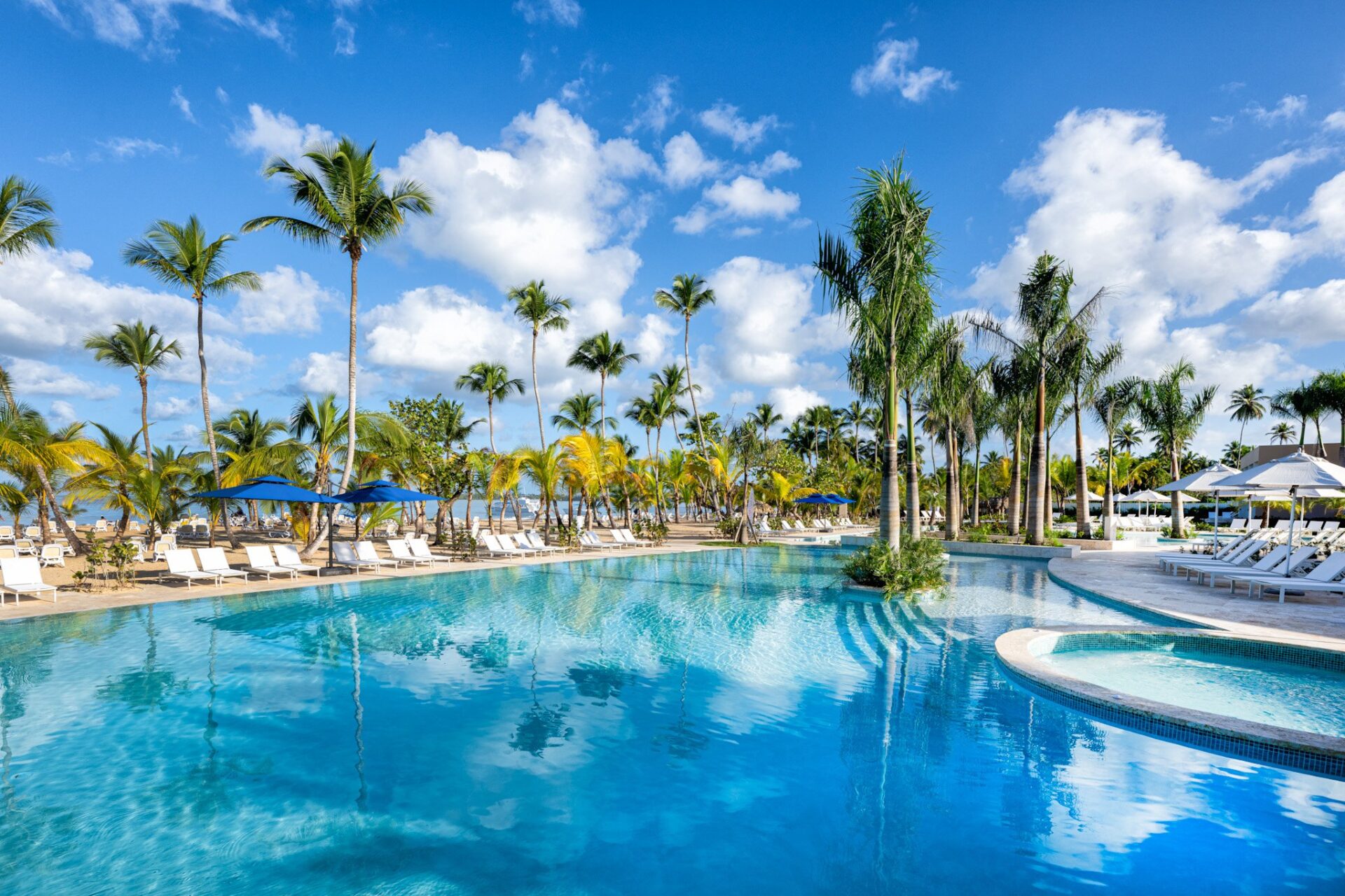 Piscina infinity rodeada de palmeras y tumbonas blancas con sombrillas azules en el resort Viva Miches By Wyndham.