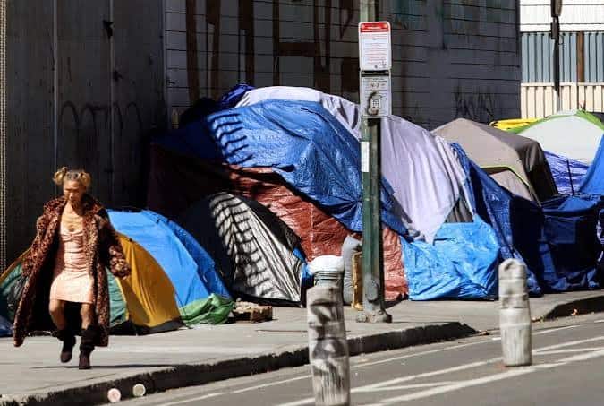 Una mujer camina junto a un campamento de personas sin hogar en una acera de Los Ángeles.