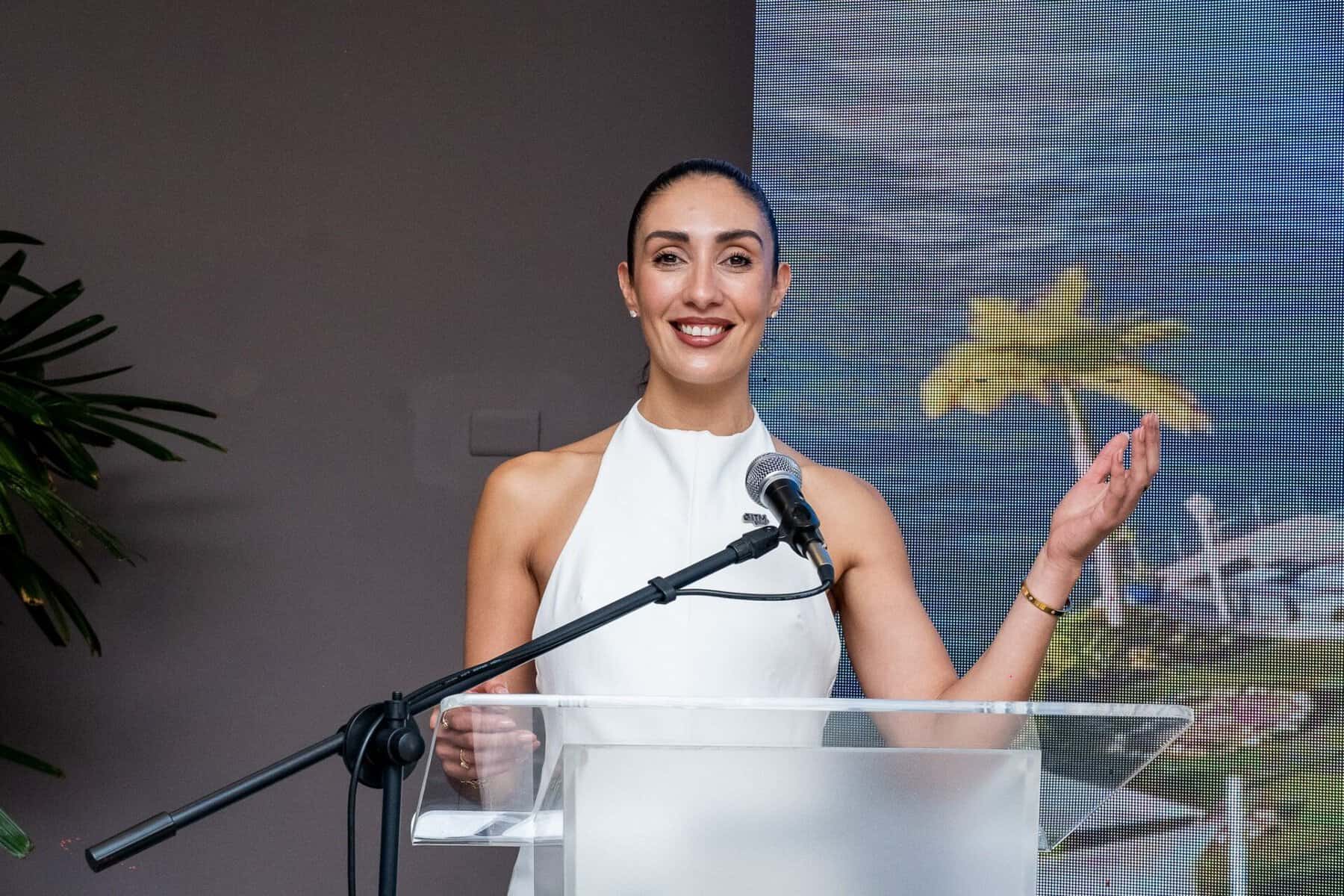 Una mujer con vestido blanco habla en un podio durante un evento turístico.